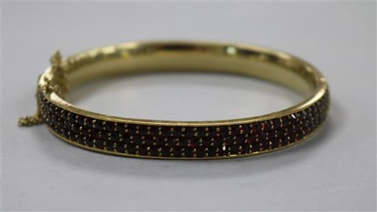 A 9ct gold and garnet encrusted hinged bangle, with safety chain.